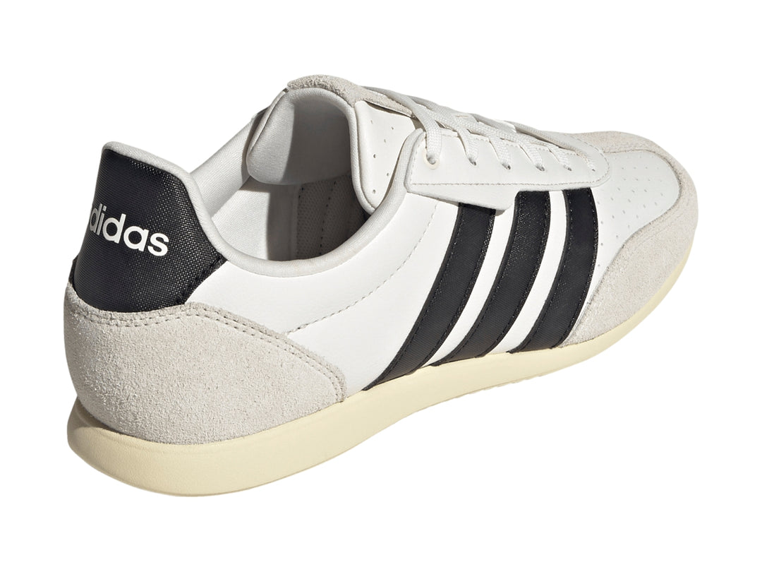 Tenis Adidas blancos con tres franjas negras y detalles en color crema en la punta y el talón.