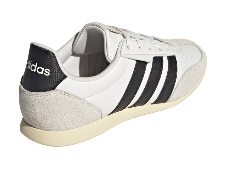 Tenis Adidas blancos con tres franjas negras y detalles en color crema en la punta y el talón.