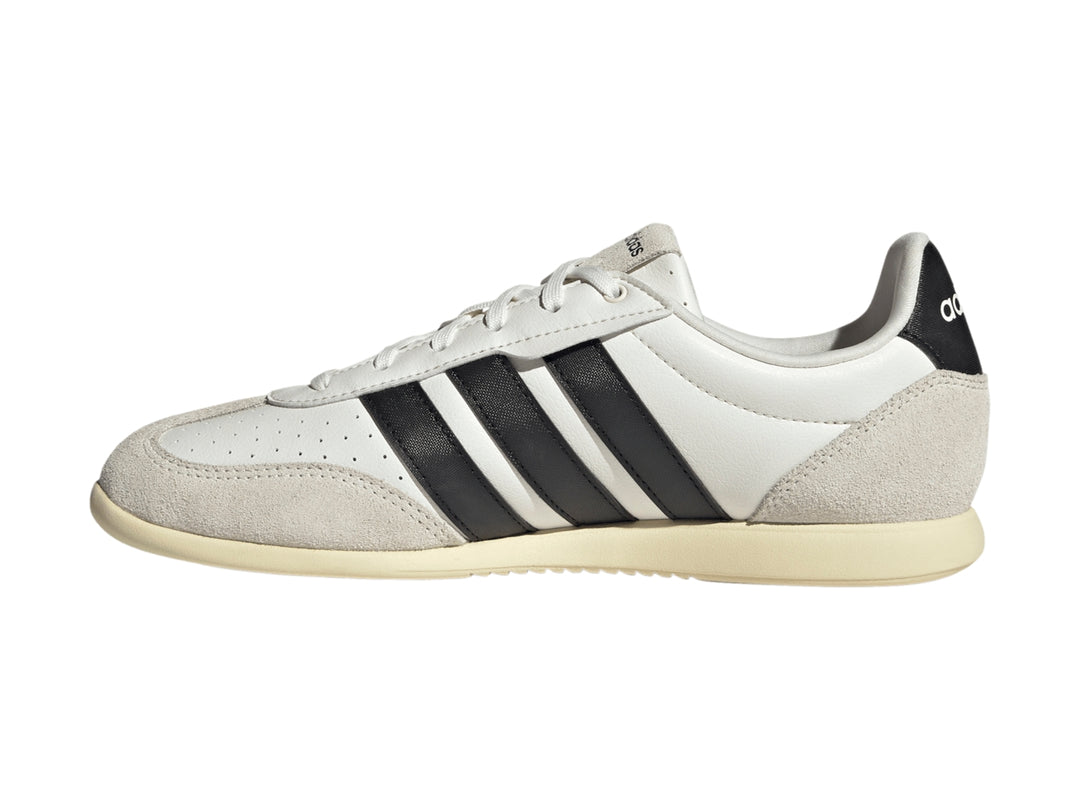 Tenis Adidas blancos con tres franjas negras y detalles en color crema en la punta y el talón.