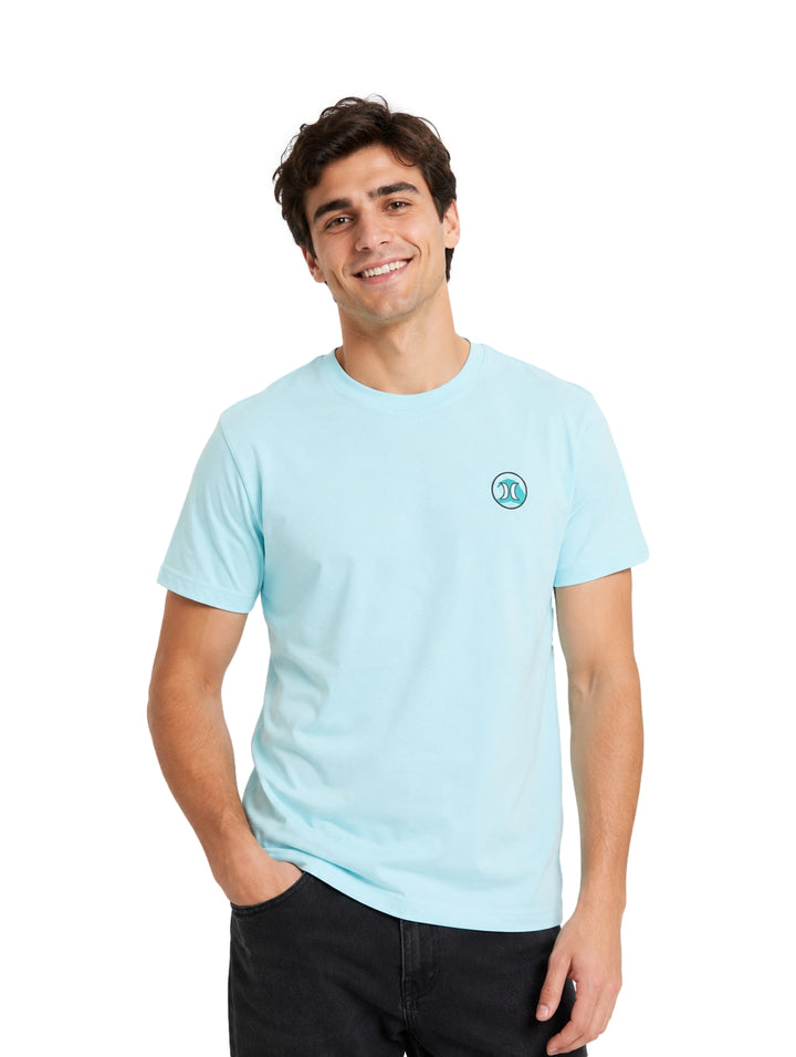 Hombre vistiendo una playera de manga corta color azul claro con un pequeño logo circular en el pecho.