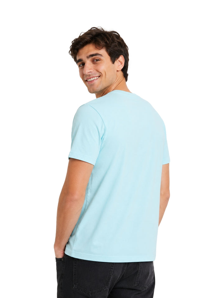 Hombre vistiendo una playera de manga corta color azul claro con un pequeño logo circular en el pecho.