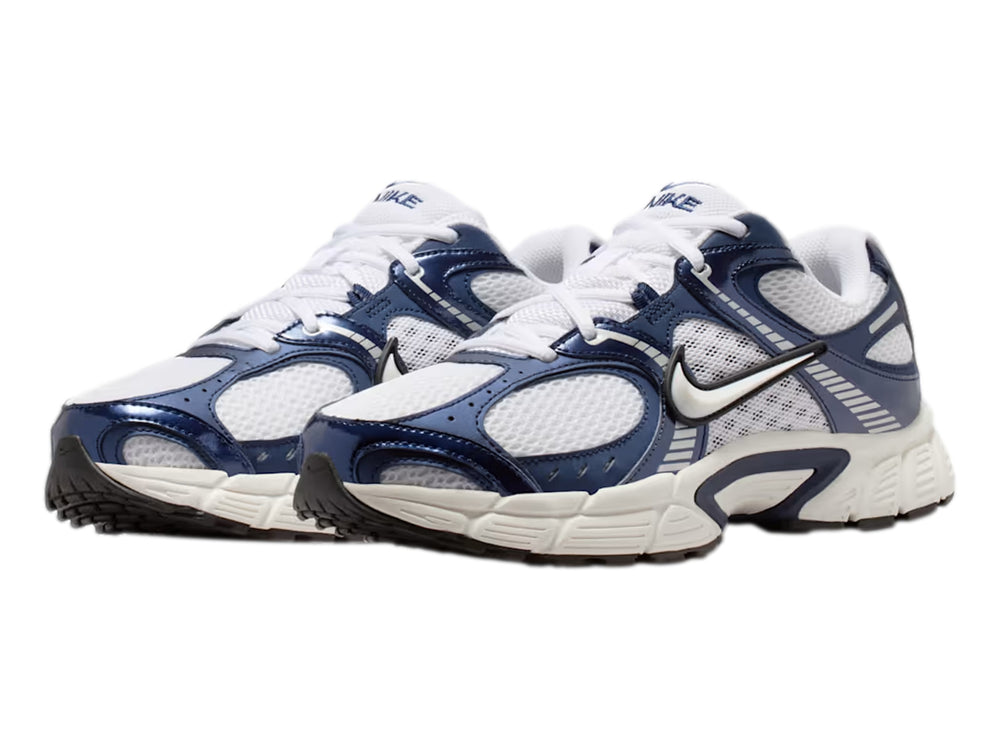 Tenis Nike color blanco y azul marino con detalles plateados y suela blanca robusta.