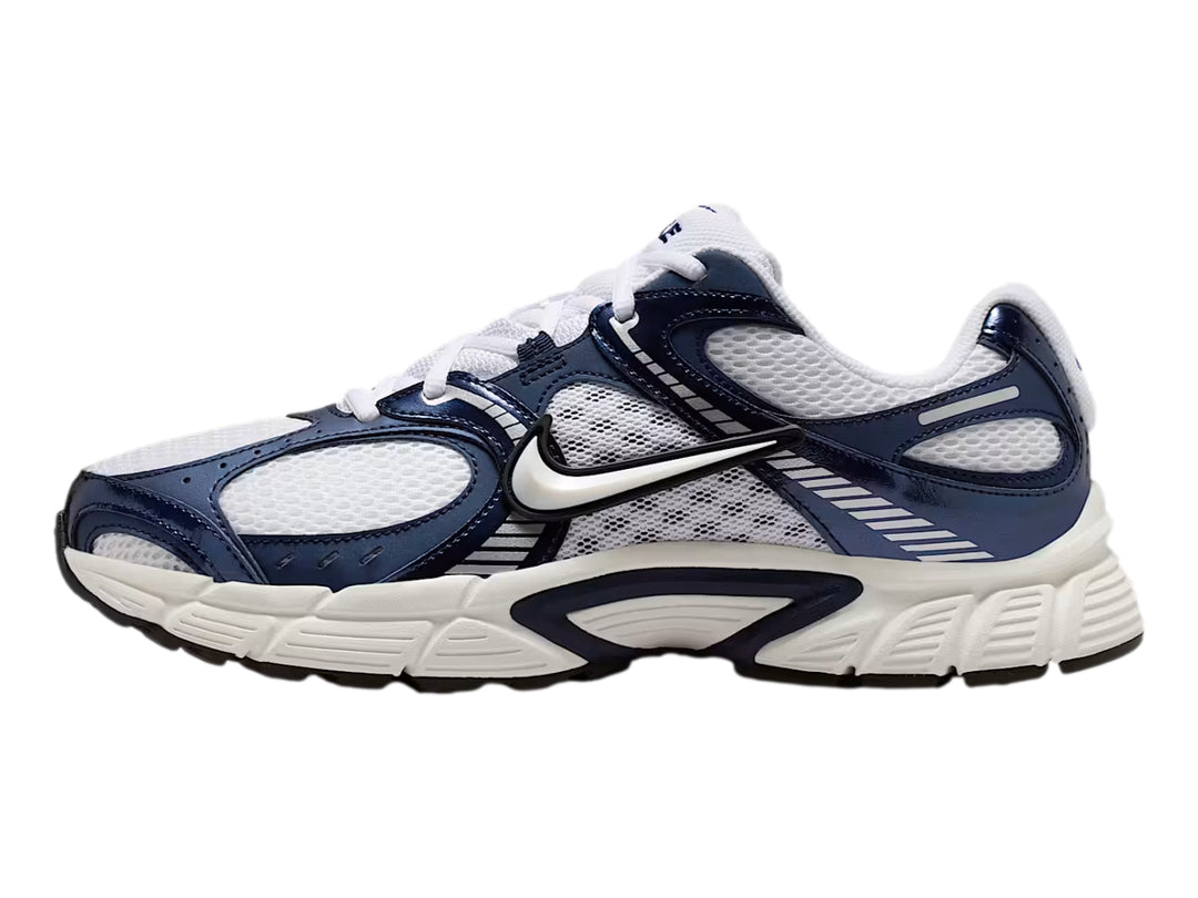 Tenis Nike color blanco y azul marino con detalles plateados y suela blanca robusta.