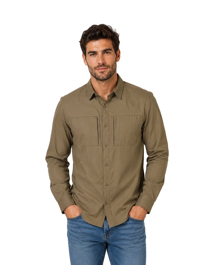 Hombre vistiendo una camisa de manga larga color oliva con bolsillos frontales y pantalones azules.