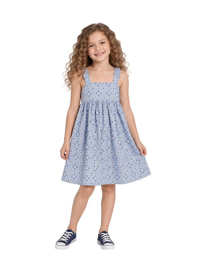 Niña vistiendo un vestido corto azul claro con estampado de flores blancas y azules, combinado con tenis azul marino.