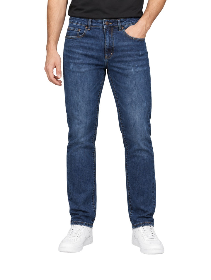 Hombre vistiendo jeans rectos de color índigo con tenis blancos sobre fondo blanco.