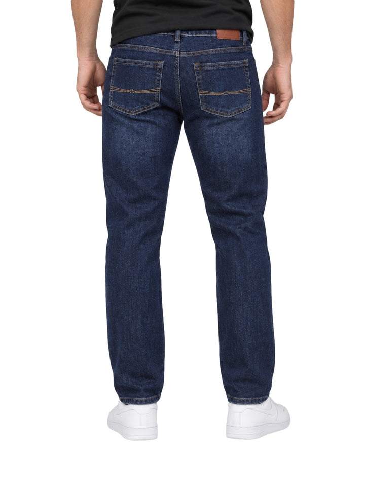 Hombre vistiendo jeans rectos de color índigo con tenis blancos sobre fondo blanco.