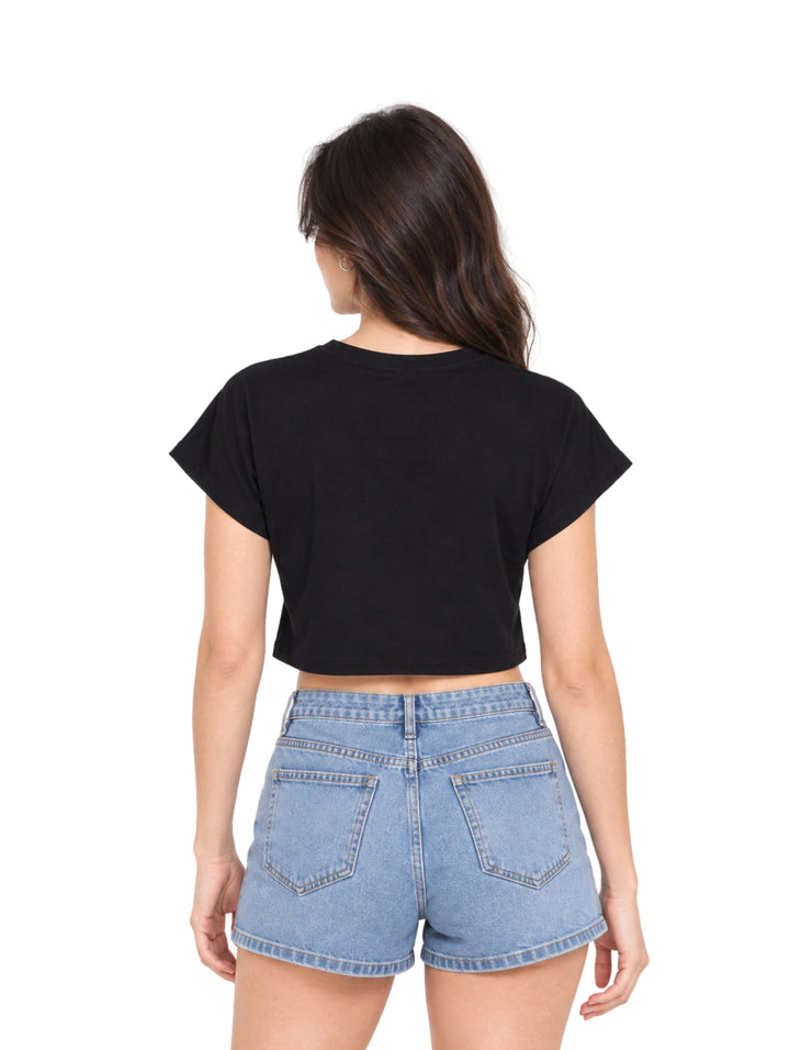 Mujer vistiendo playera crop top color negro con estampado gráfico y shorts de mezclilla azules.