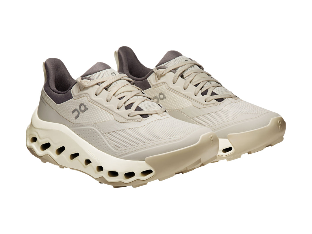 Tenis deportivos On Cloud color beige con suela gruesa y cuello en color gris oscuro.