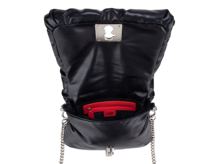 Bolso pequeño negro acolchado con correa de cadena plateada y broche decorativo.