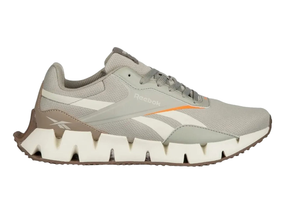 Tenis deportivos Reebok en color gris y blanco con detalles en naranja y suela blanca dentada.