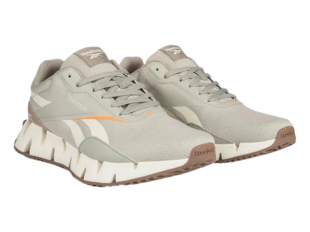 Tenis deportivos Reebok en color gris y blanco con detalles en naranja y suela blanca dentada.