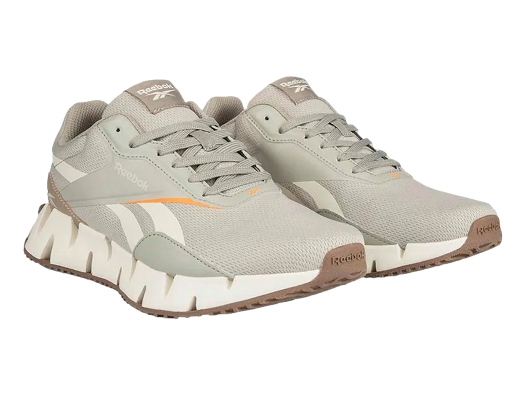 Tenis deportivos Reebok en color gris y blanco con detalles en naranja y suela blanca dentada.