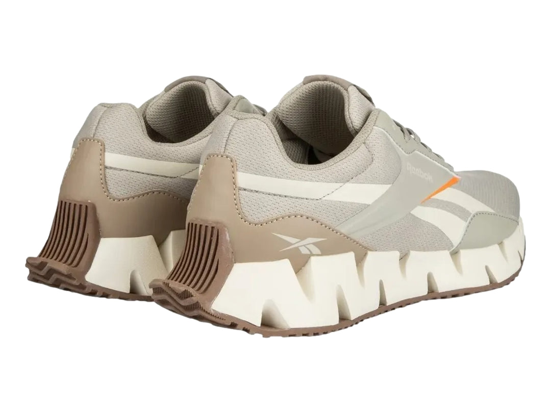 Tenis deportivos Reebok en color gris y blanco con detalles en naranja y suela blanca dentada.