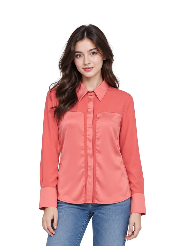 Mujer joven vistiendo una camisa color salmón de manga larga y jeans azules.