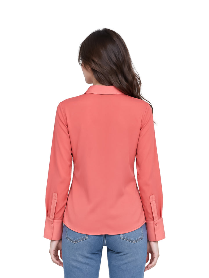 Mujer joven vistiendo una camisa color salmón de manga larga y jeans azules.