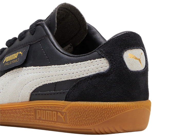 Tenis PUMA Palermo color negro con suela de goma café y franja lateral gris.