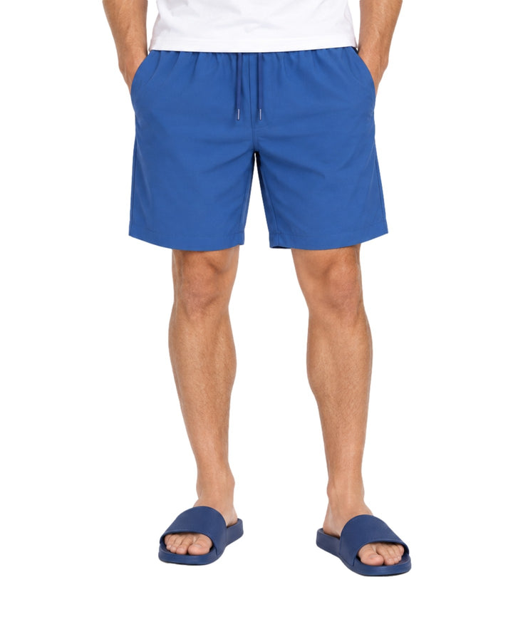 Hombre vistiendo bermuda American Fly color azul medio con cordón ajustable y sandalias azules.