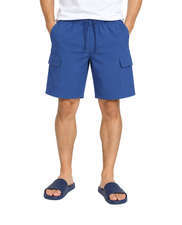 Hombre vistiendo bermuda cargo American Fly en color Medium Blue con bolsillos laterales y sandalias azules.