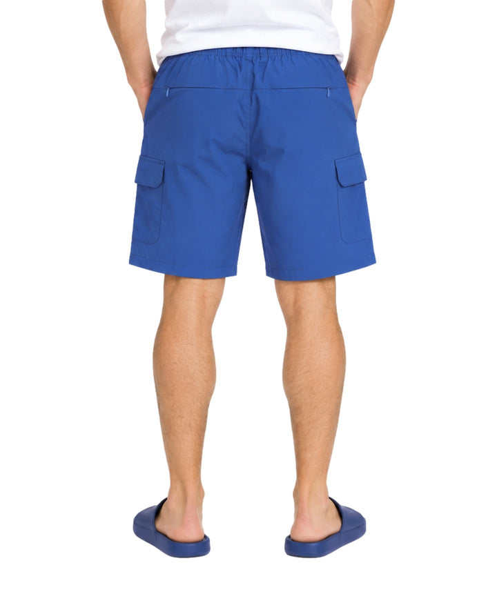 Hombre vistiendo bermuda cargo American Fly en color Medium Blue con bolsillos laterales y sandalias azules.