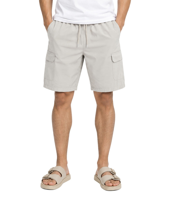 Hombre vistiendo bermuda American Fly color gris claro con bolsillos laterales y sandalias beige.