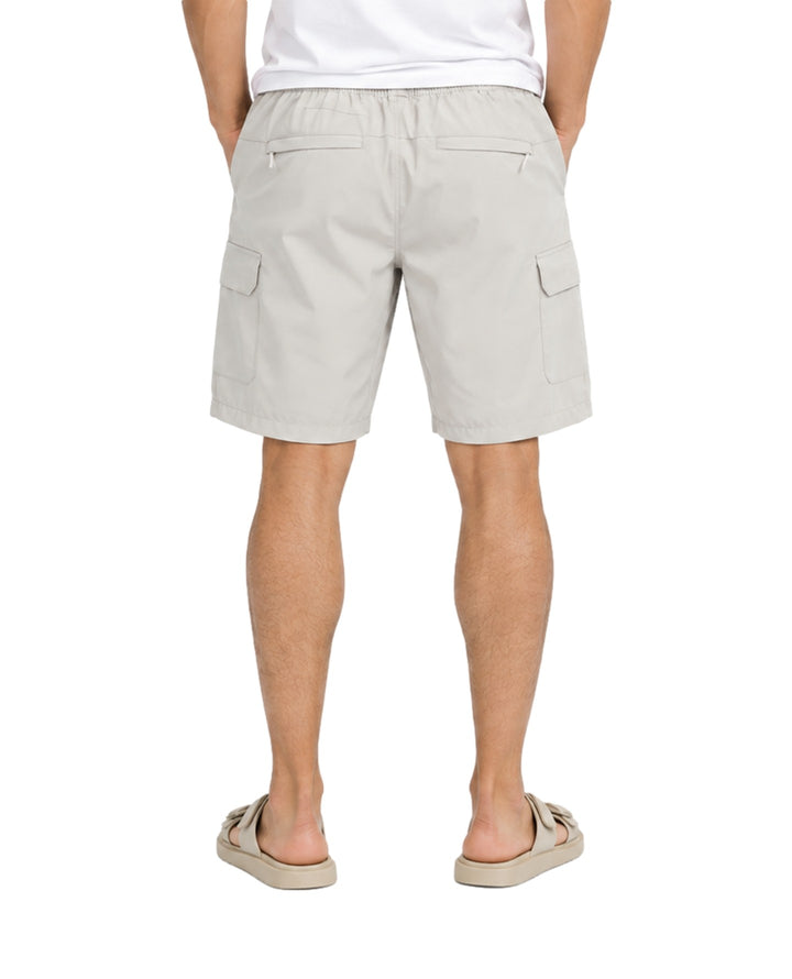 Hombre vistiendo bermuda American Fly color gris claro con bolsillos laterales y sandalias beige.