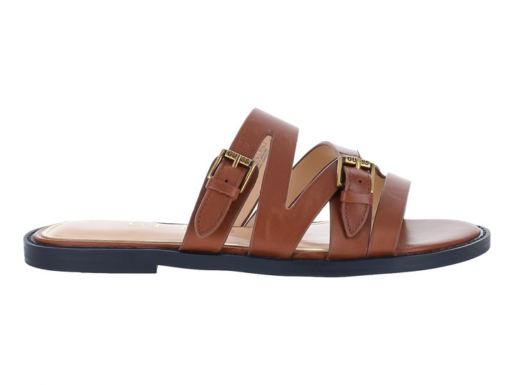 Sandalias planas color tan para mujer con correas y hebillas doradas sobre suela azul marino.