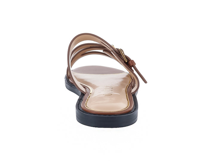Sandalias planas color tan para mujer con correas y hebillas doradas sobre suela azul marino.