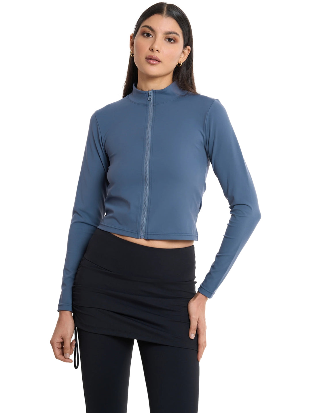 Mujer vistiendo chaqueta deportiva corta color acero con cierre frontal y leggings negros.