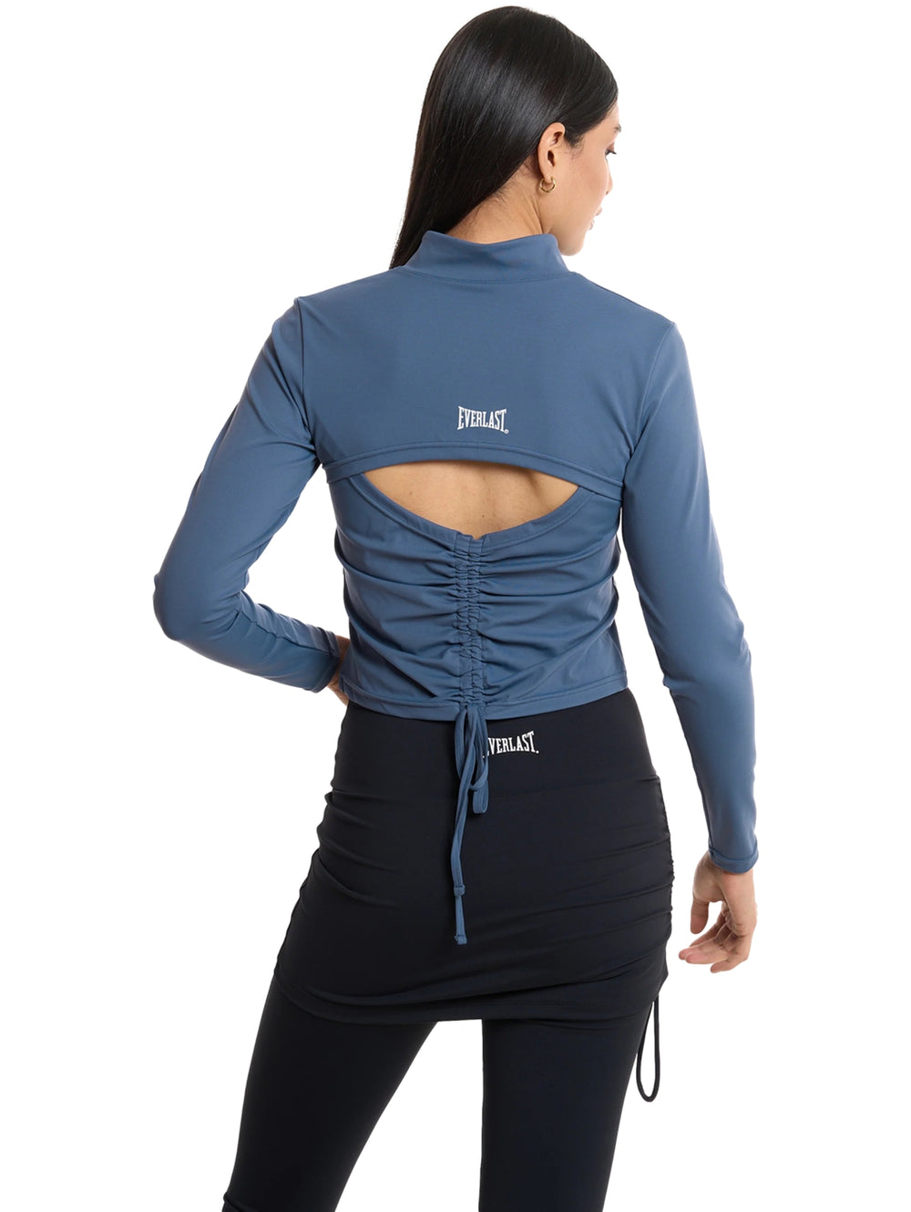 Mujer vistiendo chaqueta deportiva corta color acero con cierre frontal y leggings negros.