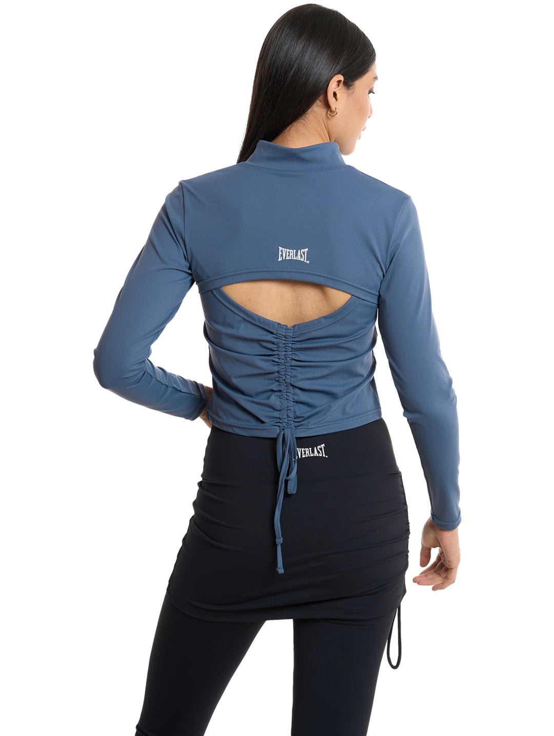 Mujer vistiendo chaqueta deportiva corta color acero con cierre frontal y leggings negros.