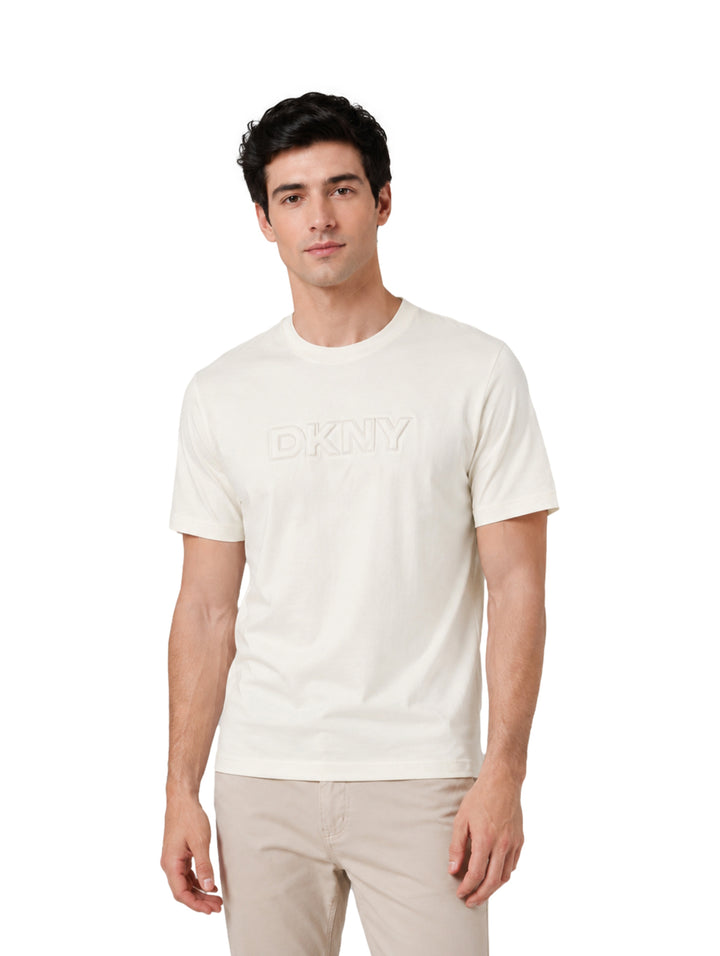 Hombre vistiendo playera de manga corta color tofu con logotipo DKNY en el pecho.