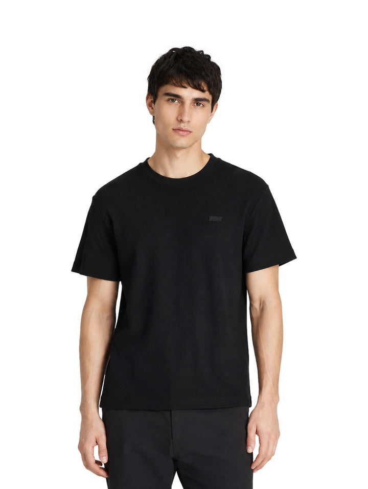Hombre vistiendo una playera DKNY de color negro con manga corta y cuello redondo.