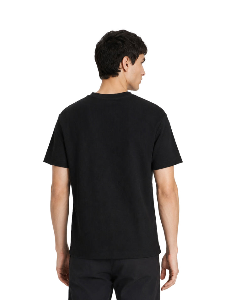 Hombre vistiendo una playera DKNY de color negro con manga corta y cuello redondo.