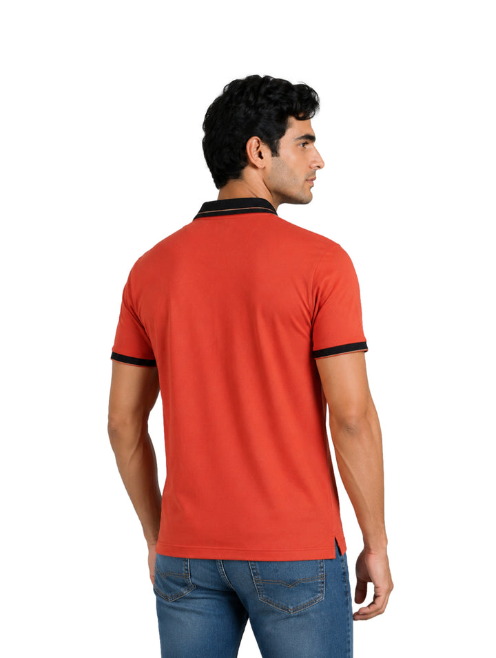 Hombre vistiendo playera polo color brick con cuello y bordes de manga en color negro.