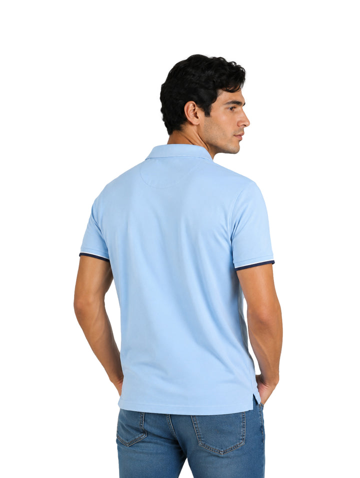 Hombre vistiendo playera polo azul claro con detalles en azul marino en el cuello y mangas.