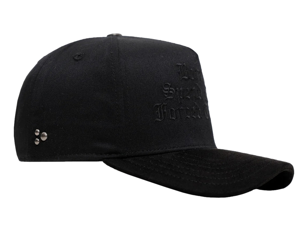 Gorra negra de JC HATS con bordado frontal y detalles metálicos laterales.