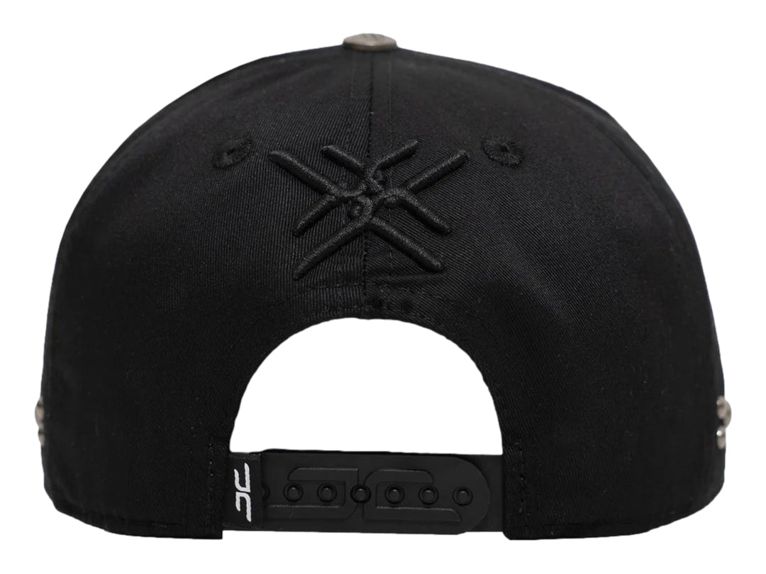 Gorra negra de JC HATS con bordado frontal y detalles metálicos laterales.