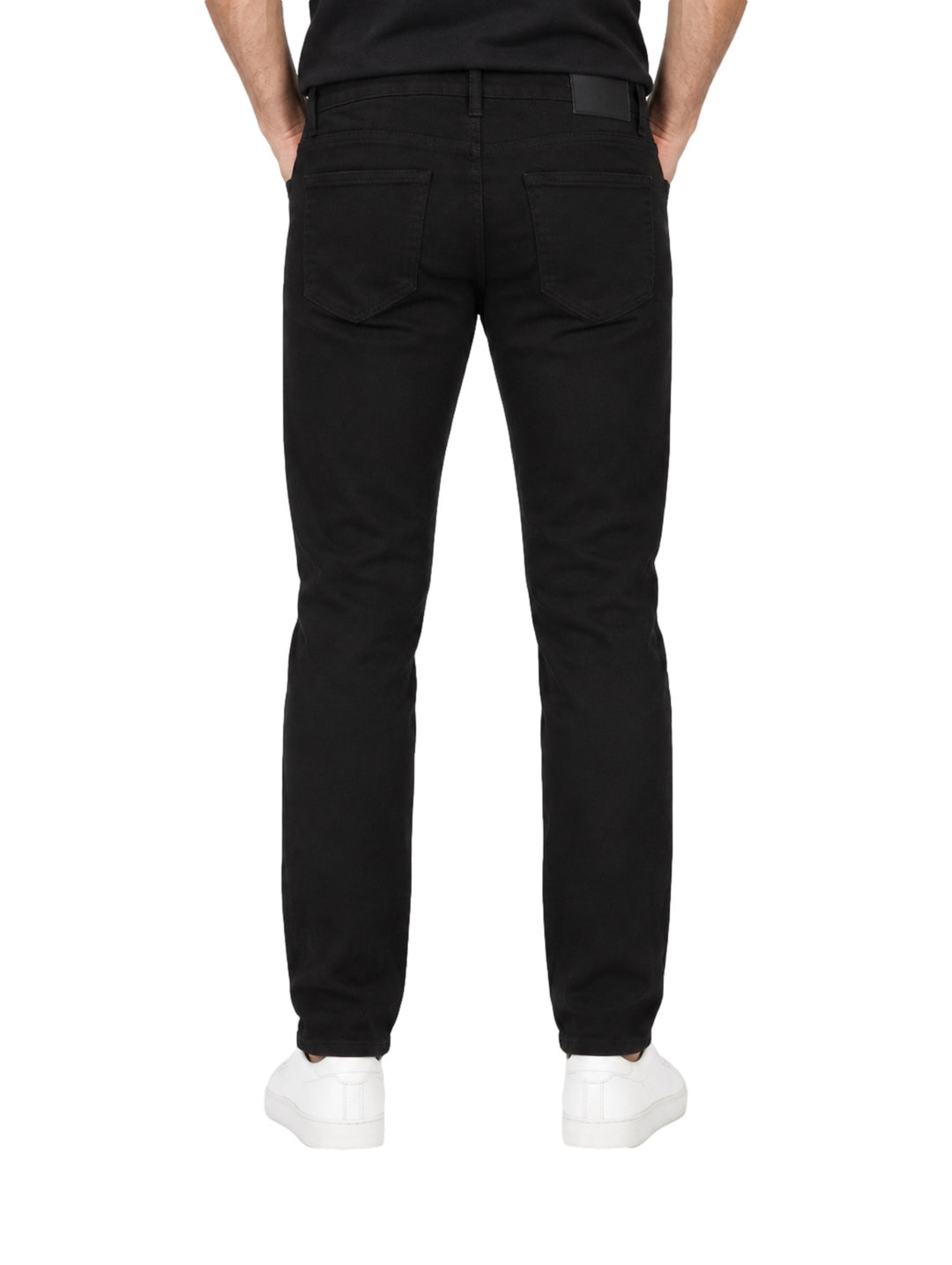 Hombre vistiendo jeans rectos de color negro con tenis blancos sobre fondo blanco.