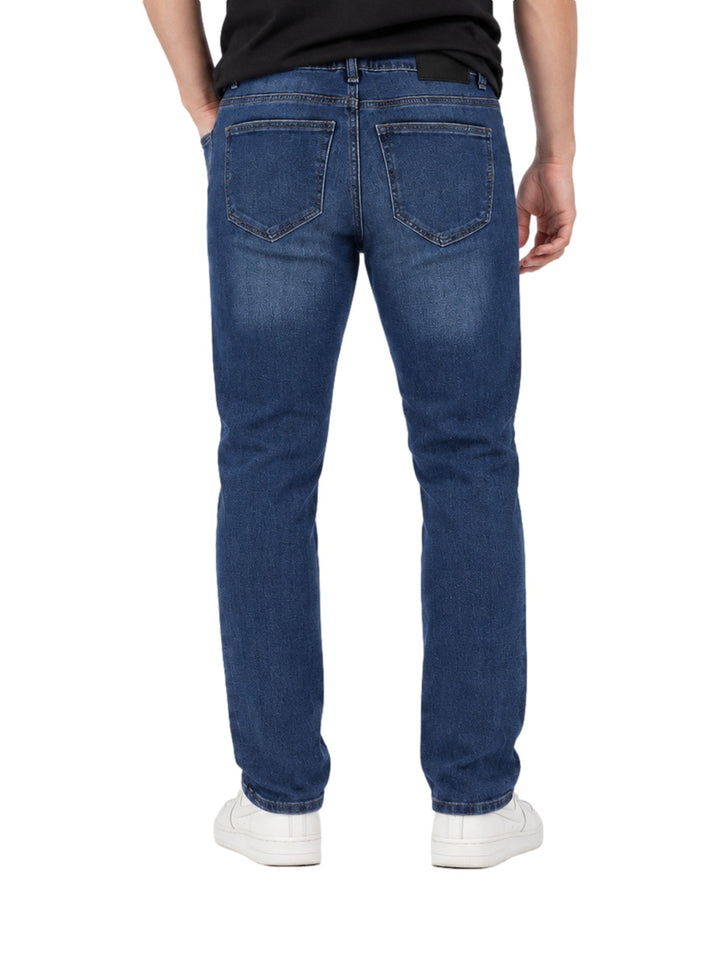 Hombre vistiendo jeans rectos color azul stone con detalles desgastados en las rodillas y tenis blancos.