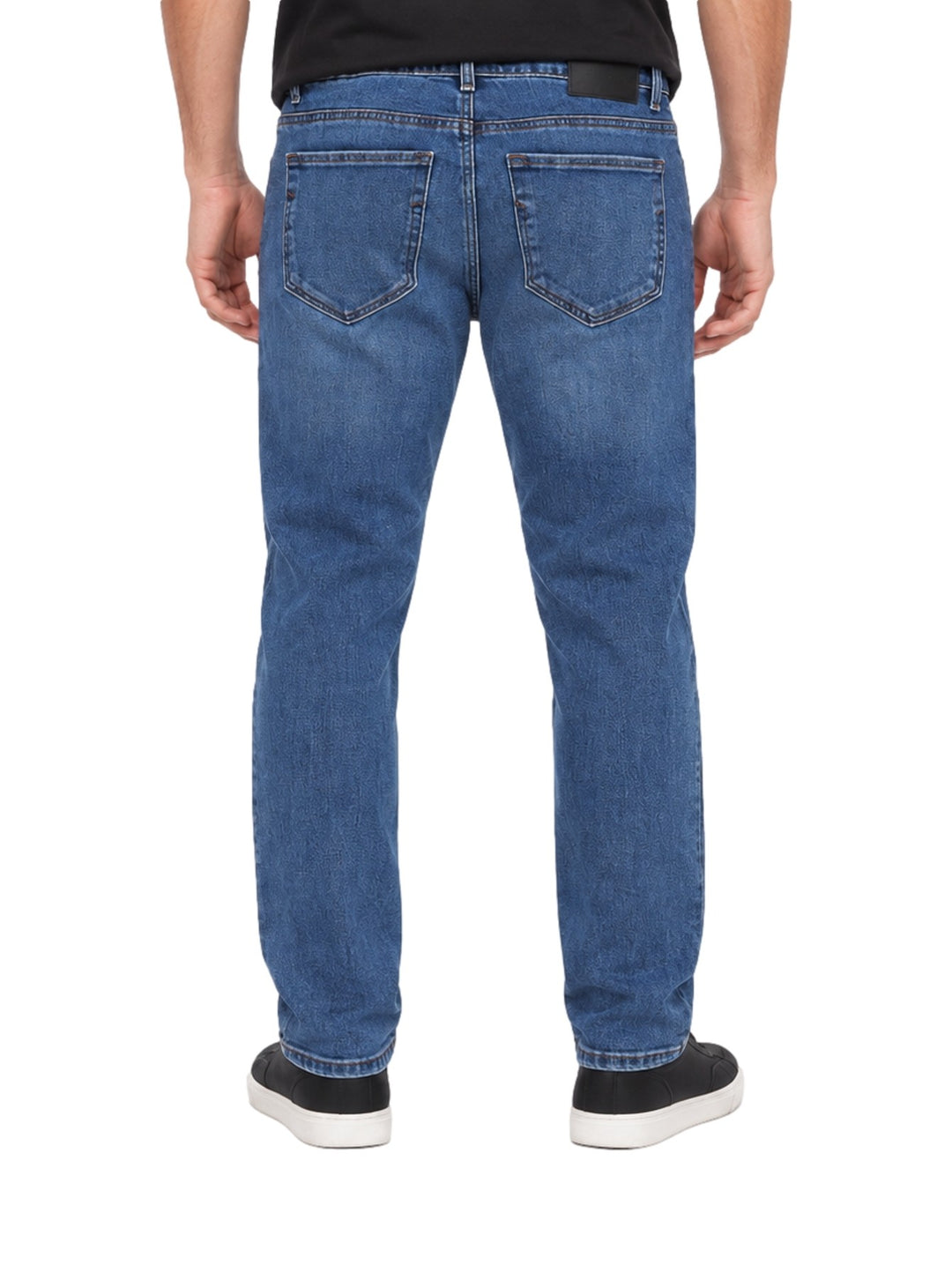 Hombre vistiendo jeans rectos de color azul stone con tenis negros sobre fondo blanco.