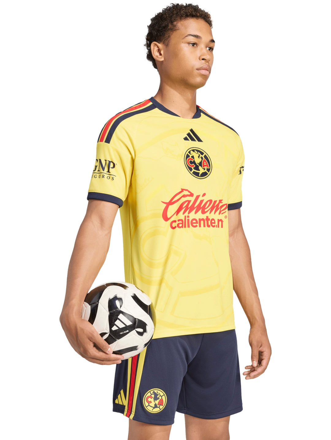 Hombre vistiendo jersey amarillo del Club América y shorts azul marino sosteniendo un balón de fútbol.