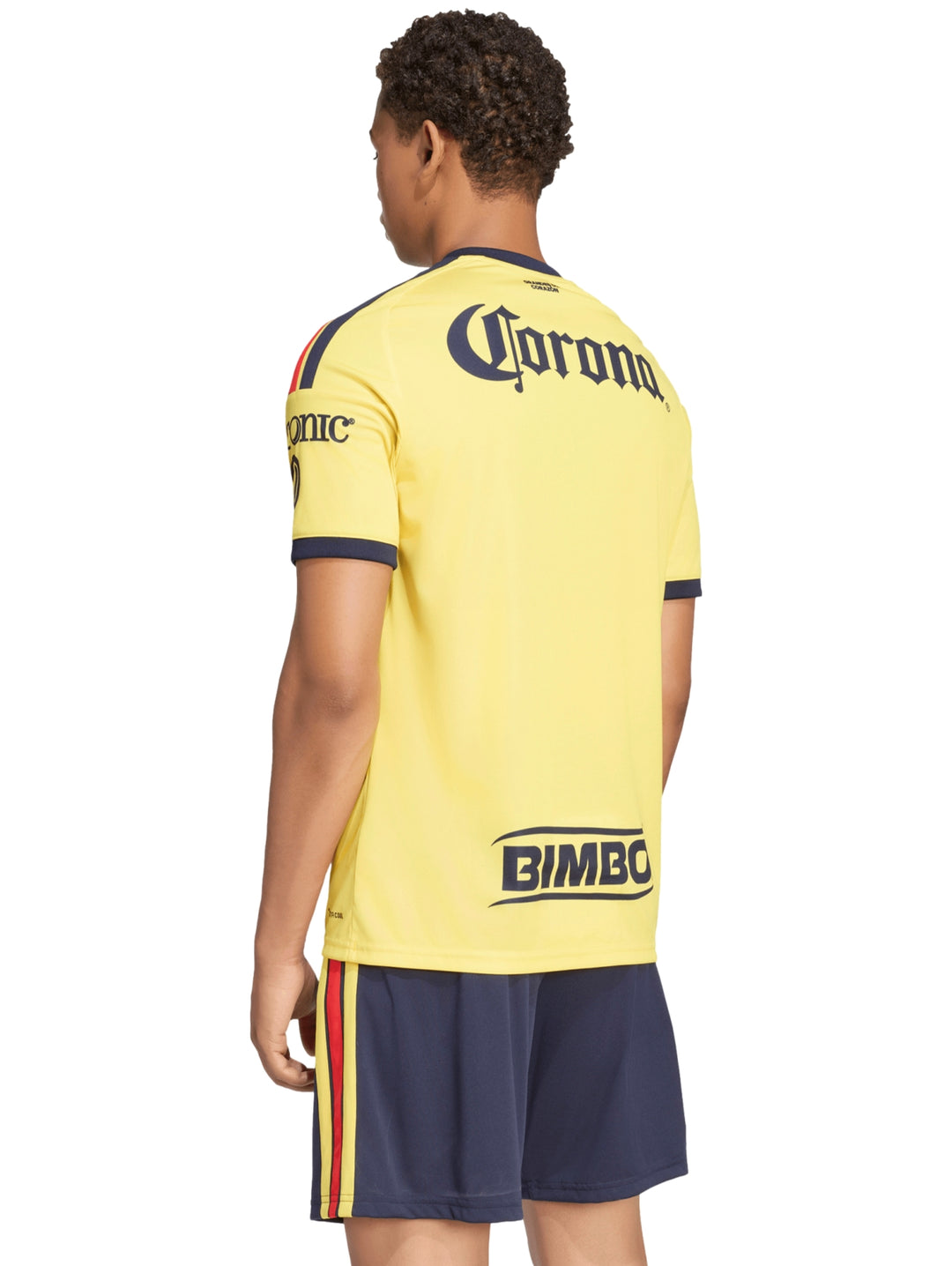 Hombre vistiendo jersey amarillo del Club América y shorts azul marino sosteniendo un balón de fútbol.