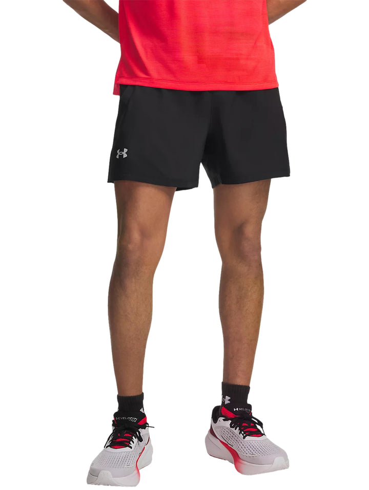 Hombre vistiendo shorts deportivos negros Under Armour, camiseta roja y calzado deportivo blanco con rojo.