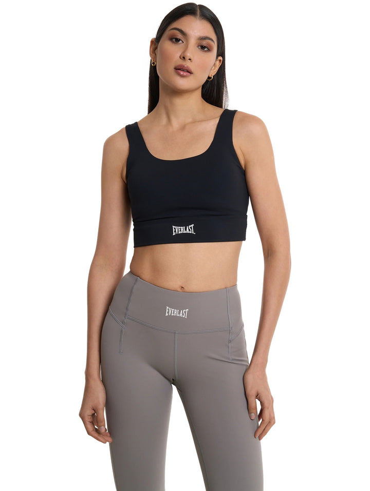 Mujer vistiendo un top deportivo corto color negro de la marca Everlast y leggings grises.