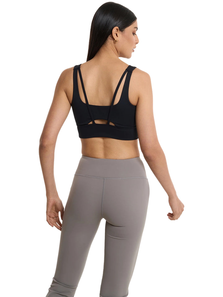 Mujer vistiendo un top deportivo corto color negro de la marca Everlast y leggings grises.