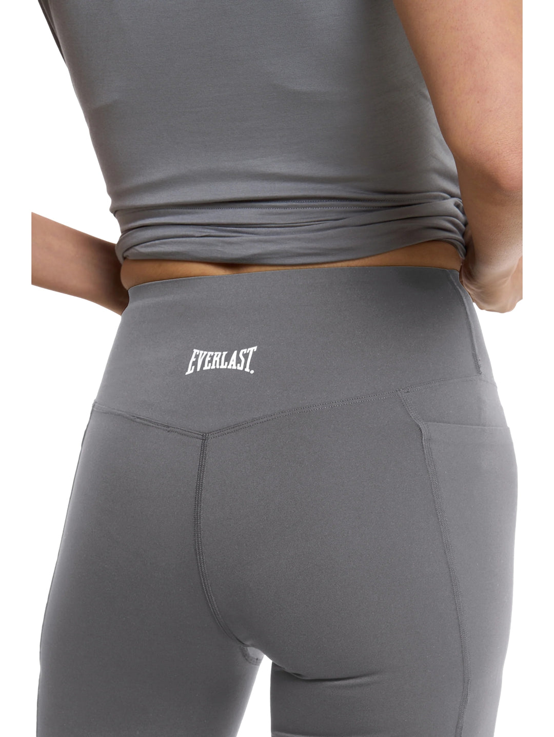 Mujer vistiendo shorts deportivos ajustados de color gris y tenis blancos sobre fondo blanco.