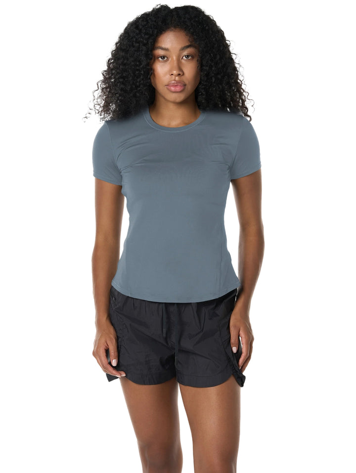 Mujer vistiendo playera deportiva azul de manga corta y shorts negros sobre fondo blanco.