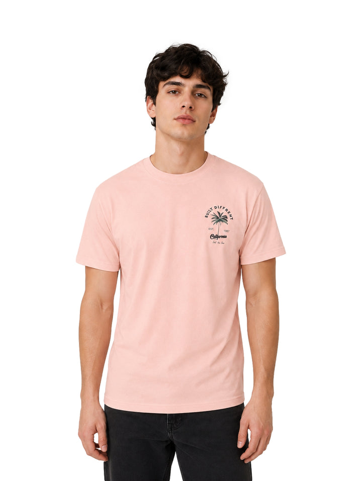 Hombre vistiendo playera de color rosa con estampado pequeño en el pecho.