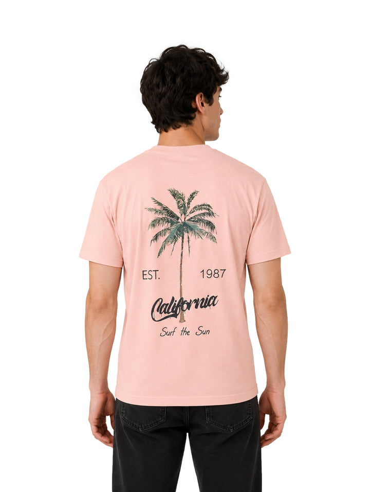Hombre vistiendo playera de color rosa con estampado pequeño en el pecho.